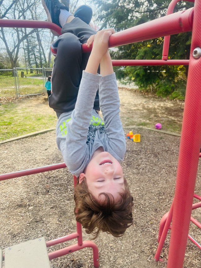 Child actively playing on natural wood playground equipment, developing gross motor skills through outdoor movement